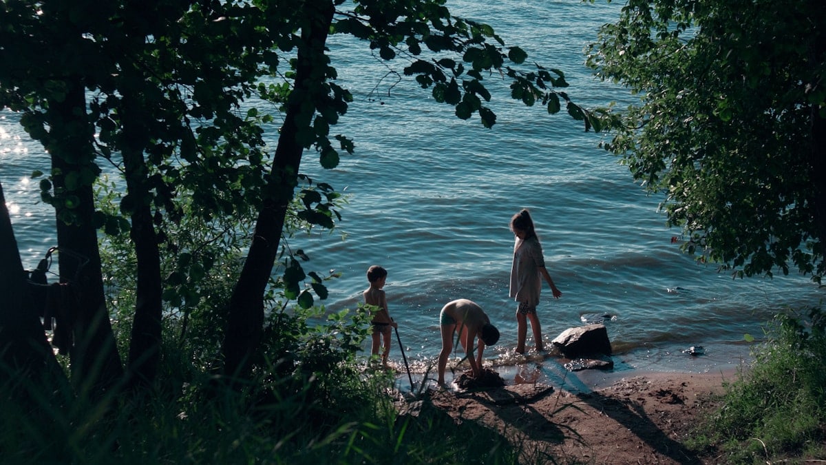 man and woman sitting on brown wooden bench near body of water during daytime
